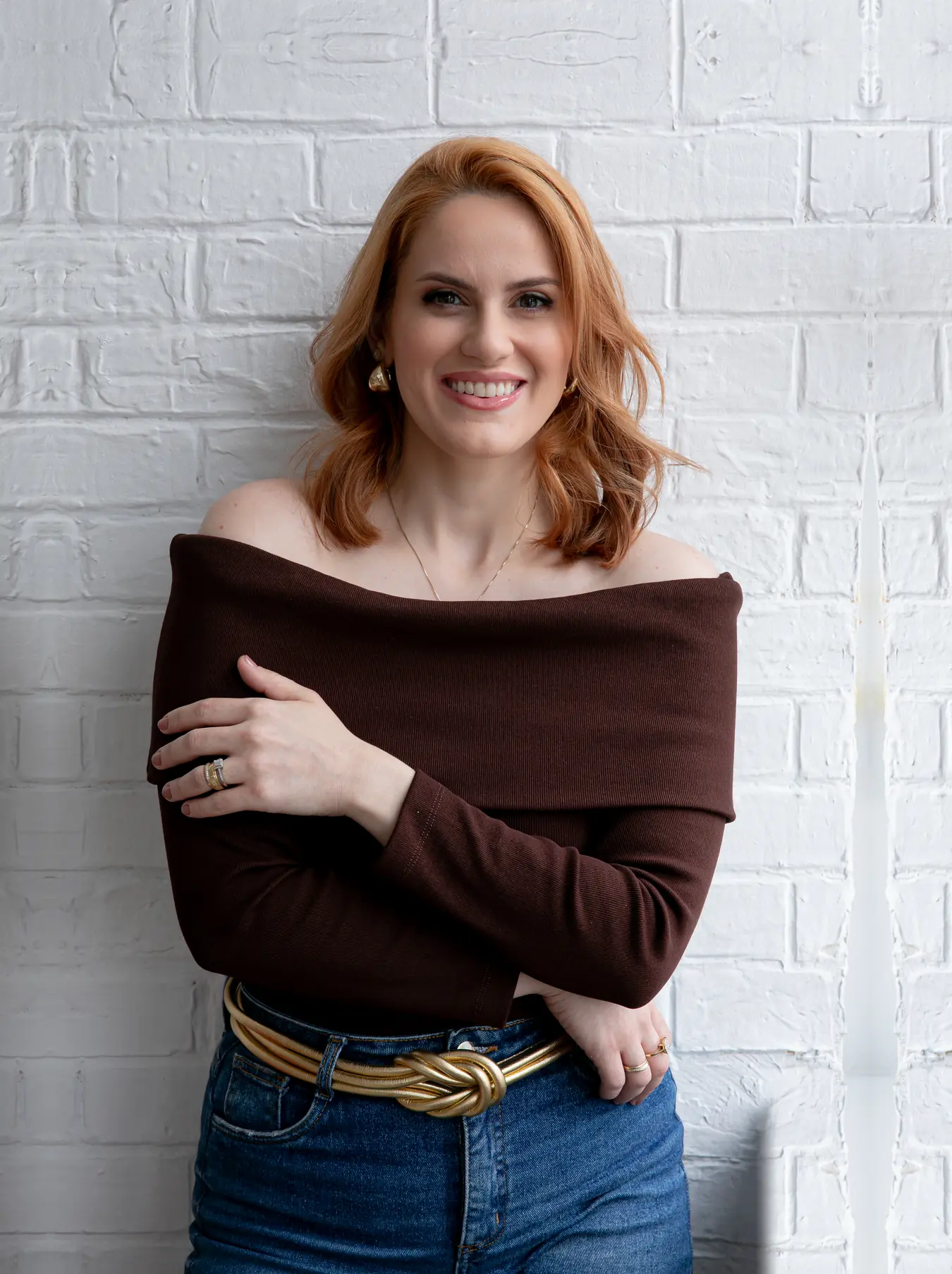 Dra. Aline Monteiro Wustro, pediatra e neonatologista, sorrindo, de braços cruzados, diante de uma parede de tijolos brancos