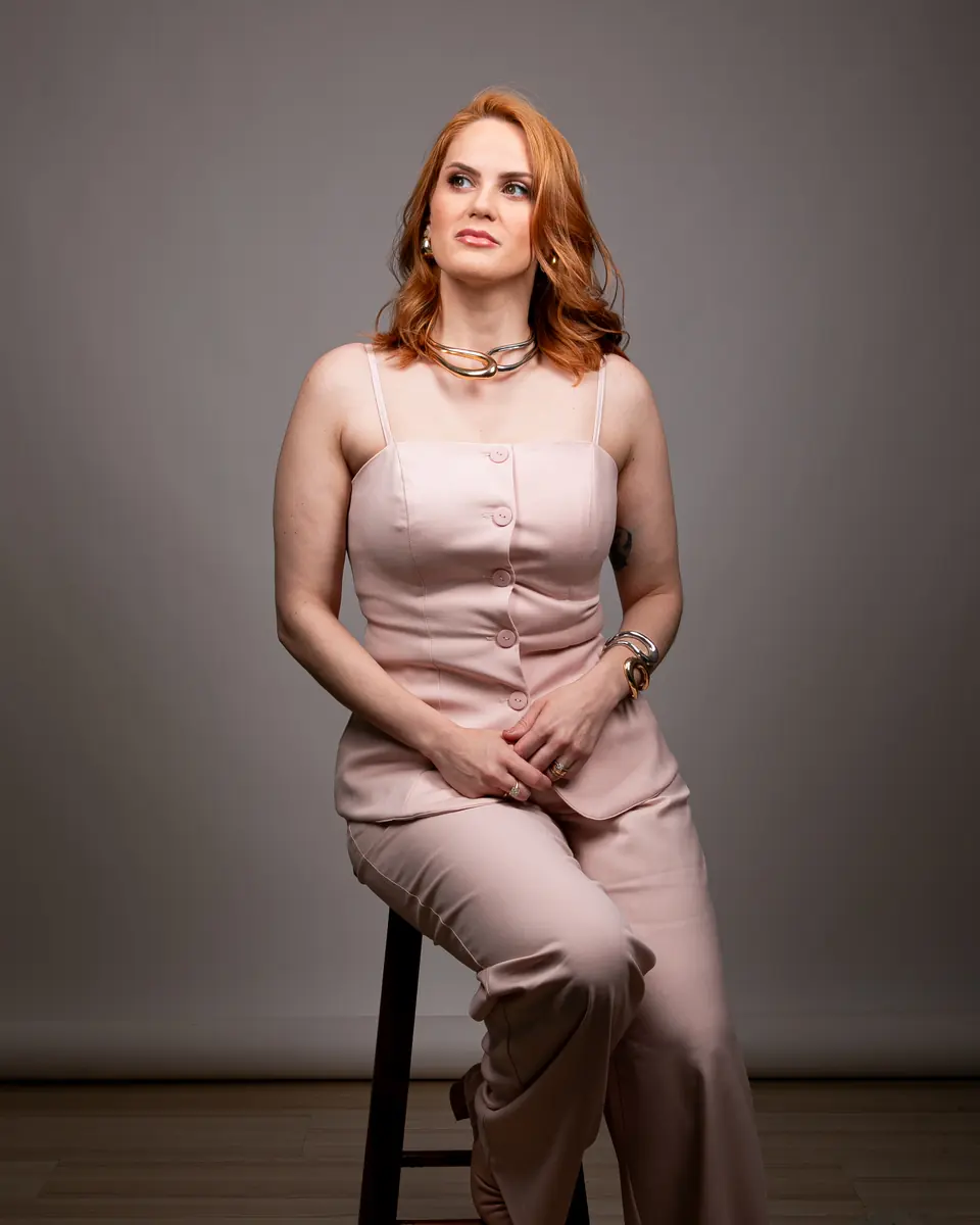Dra. Aline Monteiro Wustro sentada em um banco alto, em retrato de estúdio